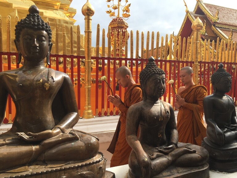 Chiang Mai Zwei gläubige Männer in typischem Gewand mit zwei großen religiösen Figuren im Vordergrund